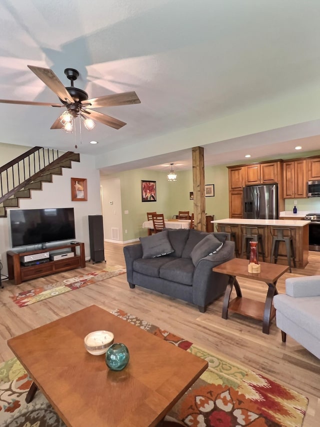 living room with ceiling fan with notable chandelier and light hardwood / wood-style floors