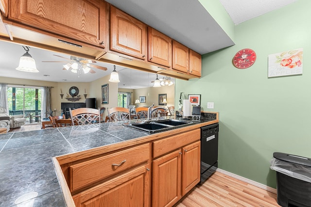 kitchen with ceiling fan, sink, dishwasher, a tile fireplace, and light hardwood / wood-style floors