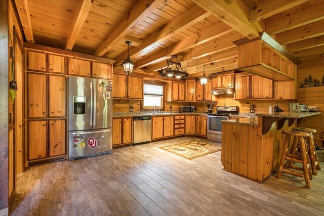 kitchen with a peninsula, appliances with stainless steel finishes, brown cabinetry, and under cabinet range hood