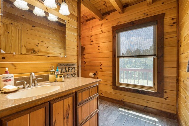 bathroom with beamed ceiling, wood finished floors, vanity, and wooden walls