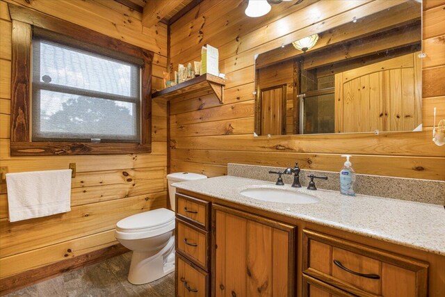 bathroom with toilet, a stall shower, wooden walls, and vanity