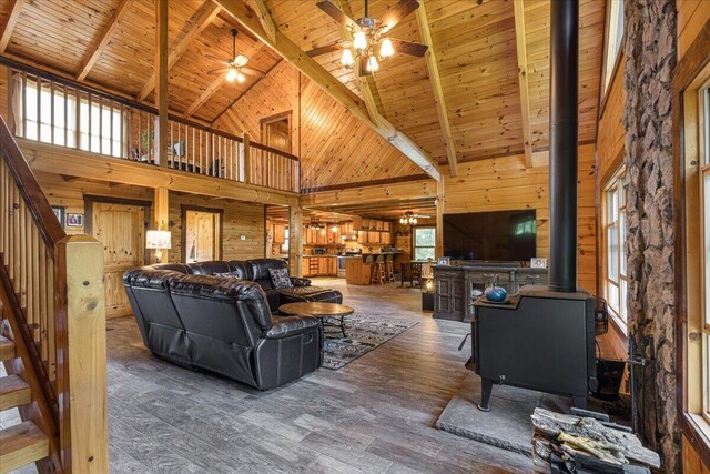 living area featuring wooden ceiling, wooden walls, wood finished floors, stairs, and a wood stove