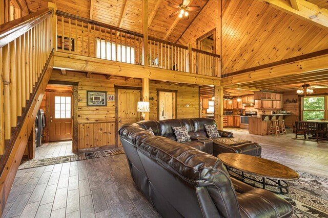 living room featuring a ceiling fan, dark wood-type flooring, wood ceiling, wooden walls, and beamed ceiling