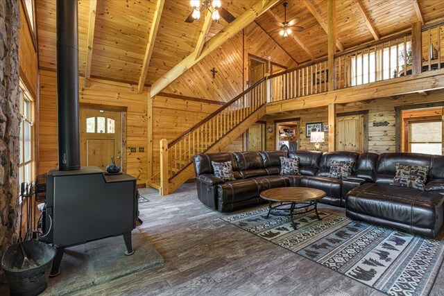 living area featuring stairway, wood walls, wooden ceiling, and a wood stove