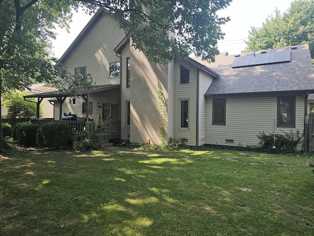 back of property with roof with shingles, roof mounted solar panels, a deck, and a lawn