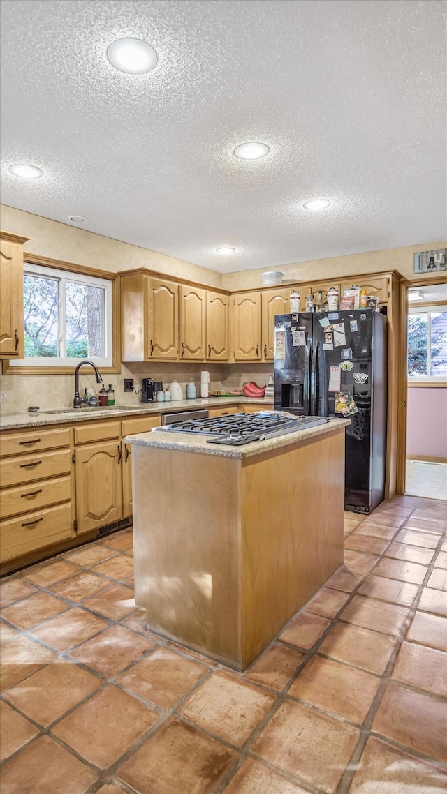 3166 W Seminole St, Springfield, MO 65807 - kitchen with black refrigerator with ice dispenser, a textured ceiling, a kitchen island, a sink, and stainless steel gas cooktop