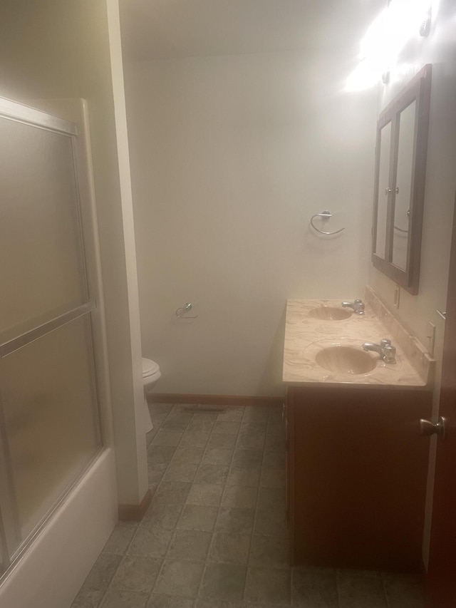bathroom with toilet, a sink, double vanity, and baseboards