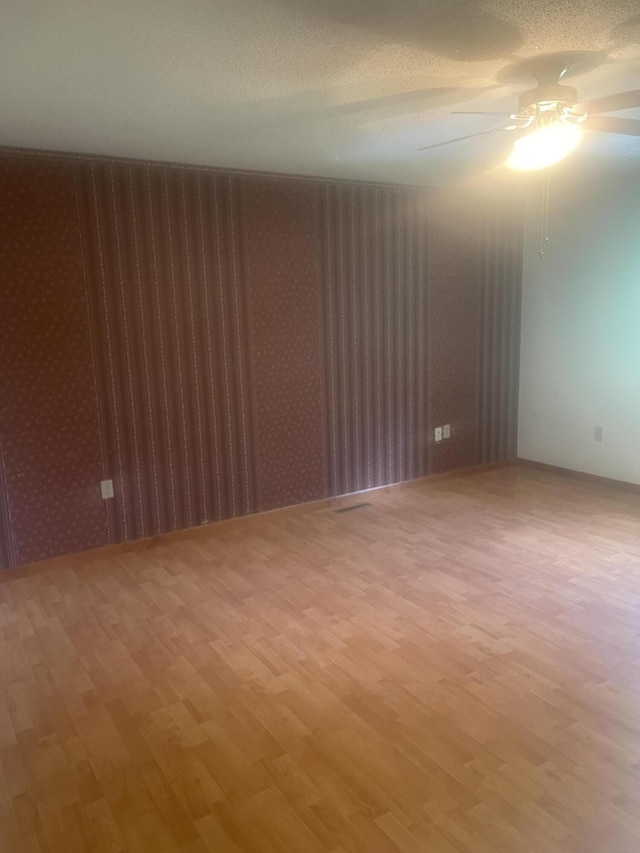 spare room featuring wallpapered walls, light wood-style flooring, and a ceiling fan