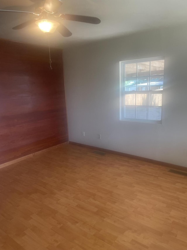 empty room featuring light wood finished floors, a ceiling fan, and baseboards