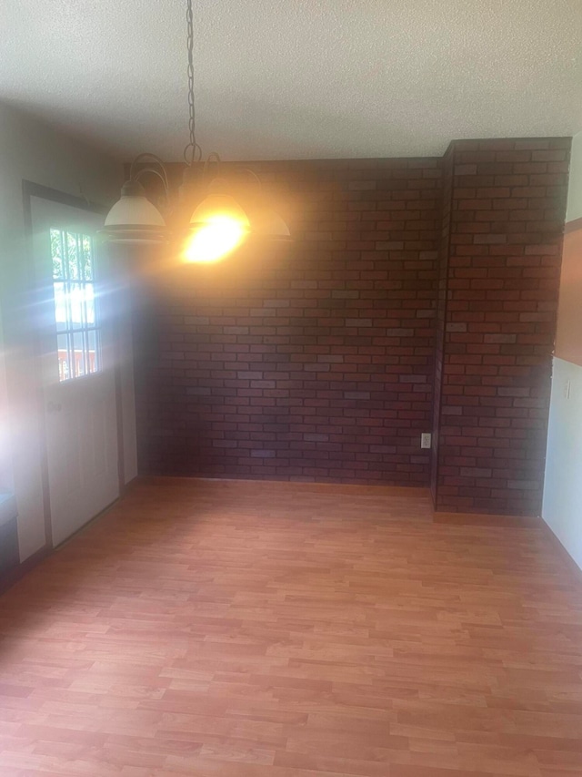 spare room featuring a chandelier, hardwood / wood-style floors, brick wall, and a textured ceiling