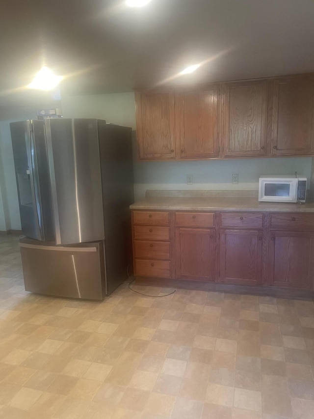 kitchen featuring brown cabinets, light floors, stainless steel fridge with ice dispenser, white microwave, and light countertops