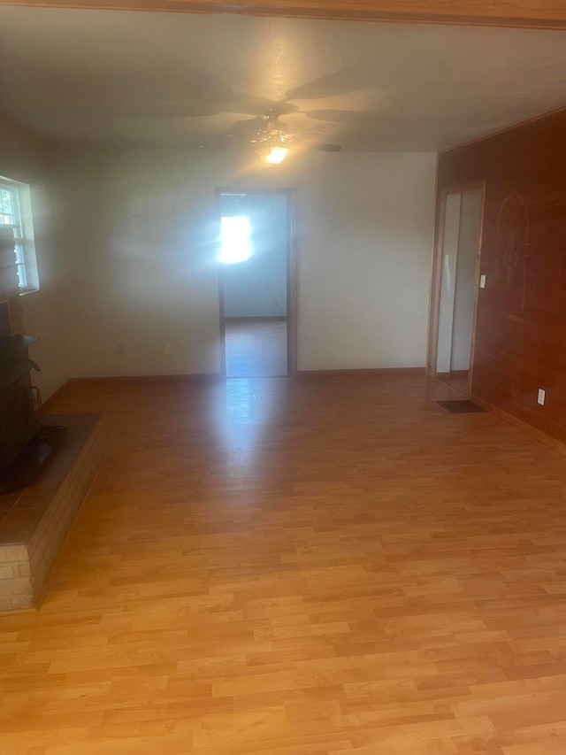 spare room featuring a wood stove, ceiling fan, and light hardwood / wood-style floors