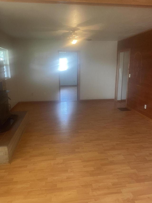empty room with light wood-style flooring, a wood stove, and a ceiling fan