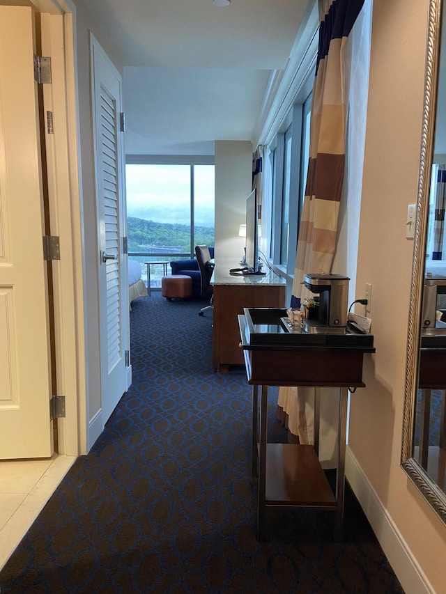 hall featuring dark carpet, expansive windows, and baseboards