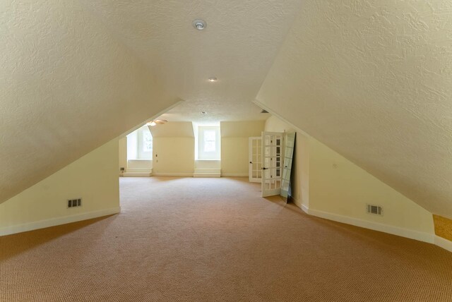 bonus room featuring lofted ceiling, light colored carpet, and a textured ceiling