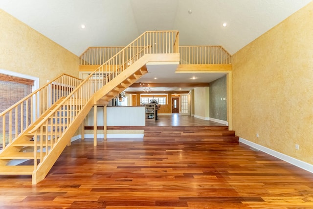 stairway with a notable chandelier, high vaulted ceiling, and hardwood / wood-style flooring