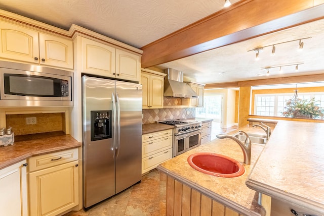 kitchen featuring wall chimney exhaust hood, cream cabinets, sink, appliances with stainless steel finishes, and a textured ceiling