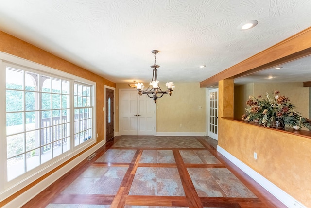 unfurnished dining area featuring a textured ceiling and a chandelier