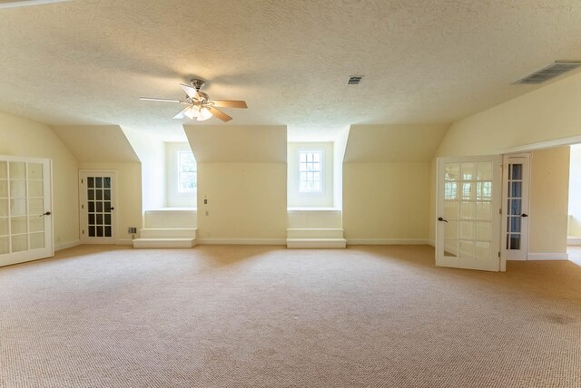 additional living space with ceiling fan, lofted ceiling, french doors, a textured ceiling, and light colored carpet