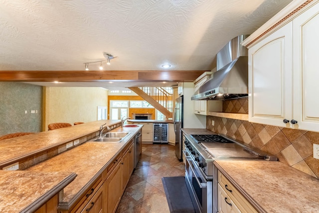 kitchen featuring sink, tasteful backsplash, a textured ceiling, wall chimney exhaust hood, and stainless steel appliances