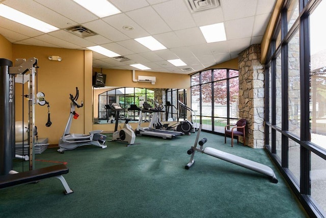 gym featuring carpet floors, plenty of natural light, an AC wall unit, and a paneled ceiling