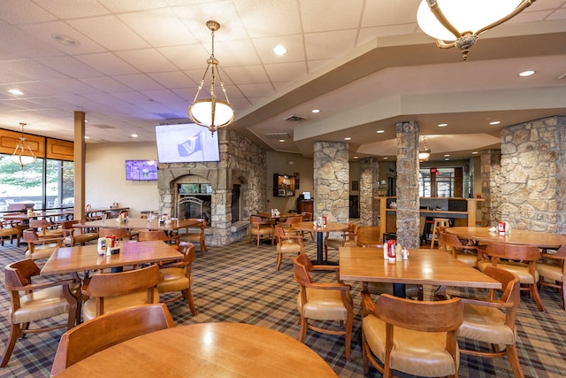 carpeted dining area featuring a stone fireplace and decorative columns