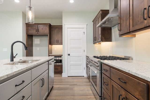 kitchen with light stone countertops, dark brown cabinetry, appliances with stainless steel finishes, wall chimney exhaust hood, and sink