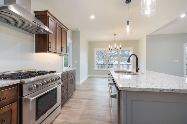 kitchen with sink, wall chimney range hood, a center island with sink, and stainless steel appliances