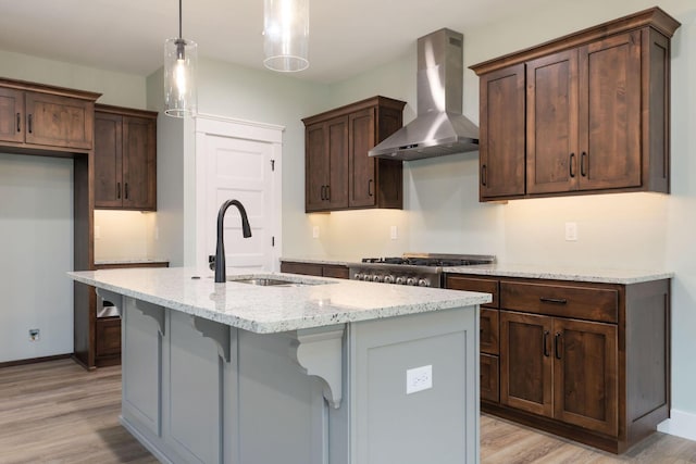 kitchen with light stone countertops, a kitchen island with sink, hanging light fixtures, and wall chimney range hood