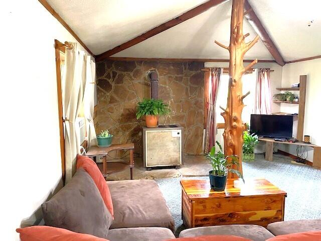 living room featuring ornamental molding, vaulted ceiling with beams, and a wood stove