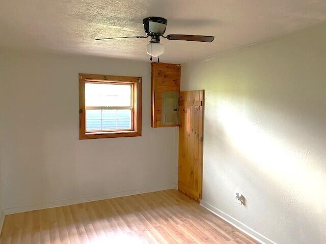 unfurnished room featuring ceiling fan, electric panel, and light hardwood / wood-style floors