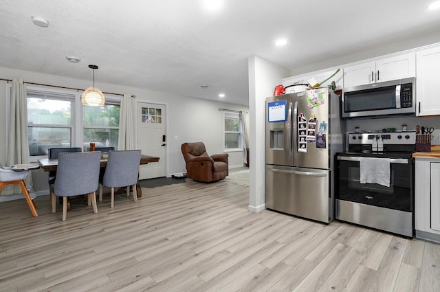 kitchen with white cabinets, light wood-type flooring, appliances with stainless steel finishes, and hanging light fixtures