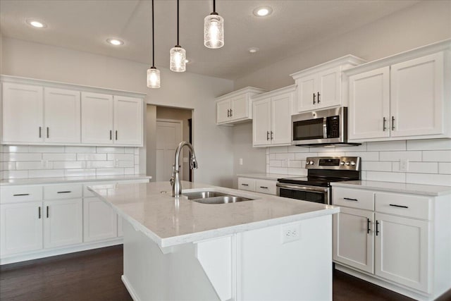 kitchen with stainless steel appliances, pendant lighting, white cabinets, and an island with sink