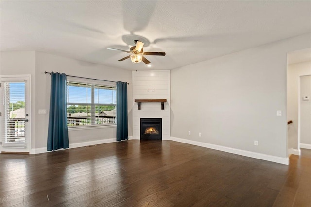 unfurnished living room featuring a healthy amount of sunlight, ceiling fan, a large fireplace, and dark hardwood / wood-style floors