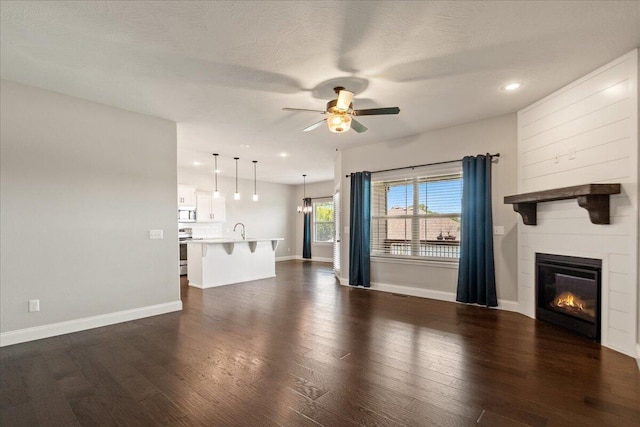 unfurnished living room featuring ceiling fan, sink, dark hardwood / wood-style floors, and a textured ceiling