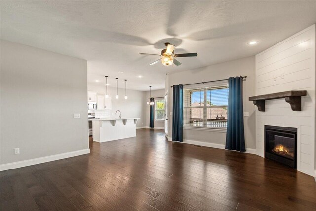 1641 N Pinnacle Ave, Nixa, MO 65714 - unfurnished living room with a sink, baseboards, ceiling fan, a fireplace, and dark wood-type flooring