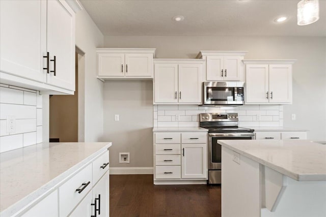 kitchen with light stone counters, white cabinets, dark hardwood / wood-style flooring, appliances with stainless steel finishes, and decorative light fixtures