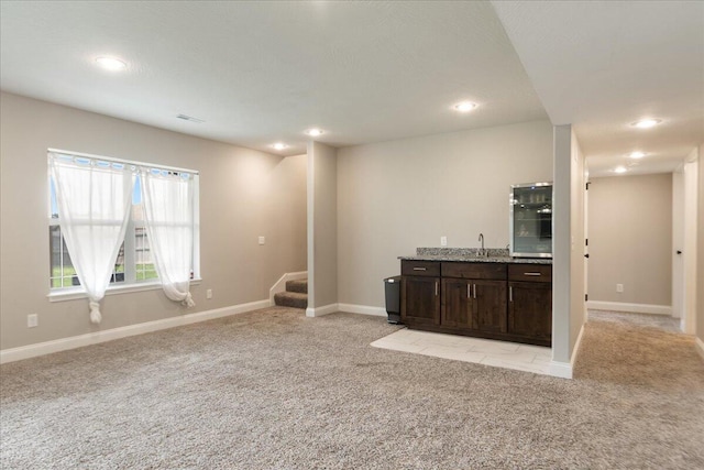 interior space featuring light stone counters, dark brown cabinetry, sink, and light colored carpet