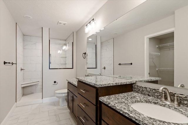 bathroom with a tile shower, vanity, and toilet