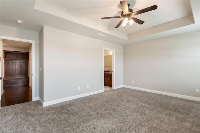 unfurnished bedroom with carpet flooring, ceiling fan, connected bathroom, and a raised ceiling