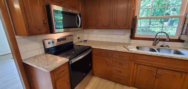 kitchen with light stone countertops, stainless steel appliances, sink, and light hardwood / wood-style flooring