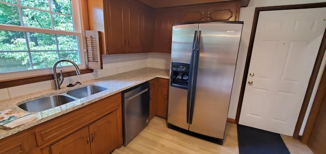 kitchen with light stone countertops, stainless steel appliances, tasteful backsplash, sink, and light hardwood / wood-style floors