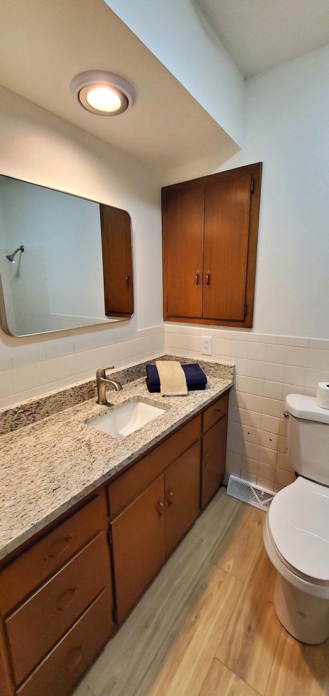 bathroom featuring wood-type flooring, vanity, tile walls, and toilet