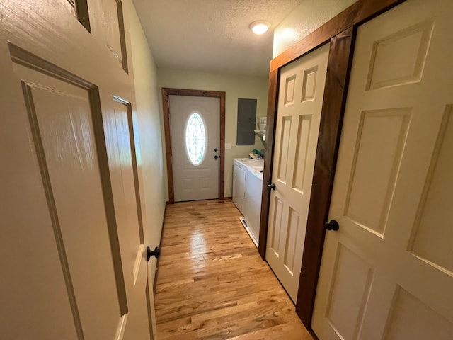 doorway to outside with electric panel, washing machine and clothes dryer, light hardwood / wood-style flooring, and a textured ceiling