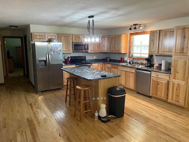 kitchen featuring a kitchen island, stainless steel appliances, sink, pendant lighting, and light hardwood / wood-style flooring