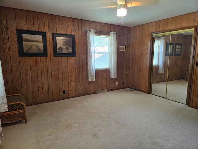 unfurnished bedroom featuring light carpet, a closet, wooden walls, and ceiling fan