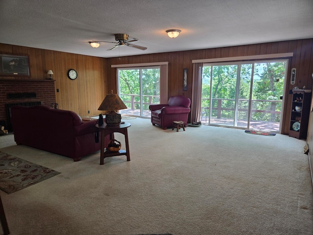 carpeted living room featuring a fireplace, ceiling fan, wood walls, and a textured ceiling