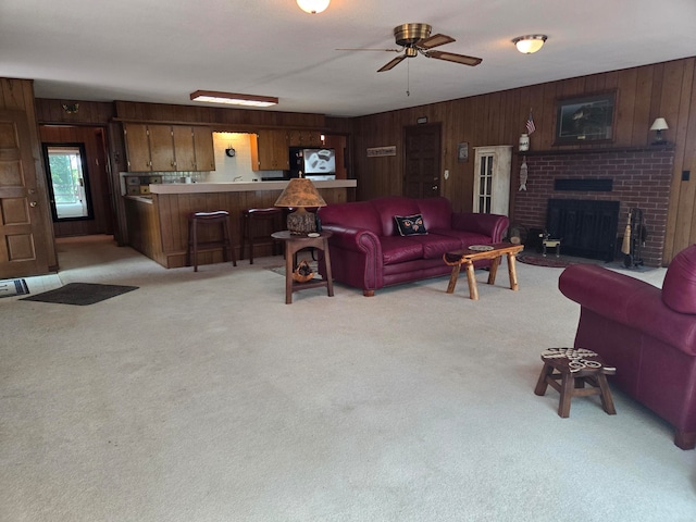 living room with ceiling fan, light colored carpet, wooden walls, and a fireplace