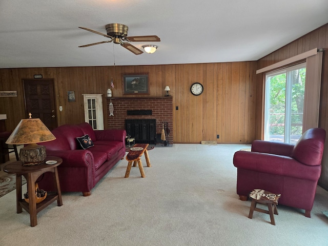 carpeted living room with ceiling fan, a fireplace, and wood walls