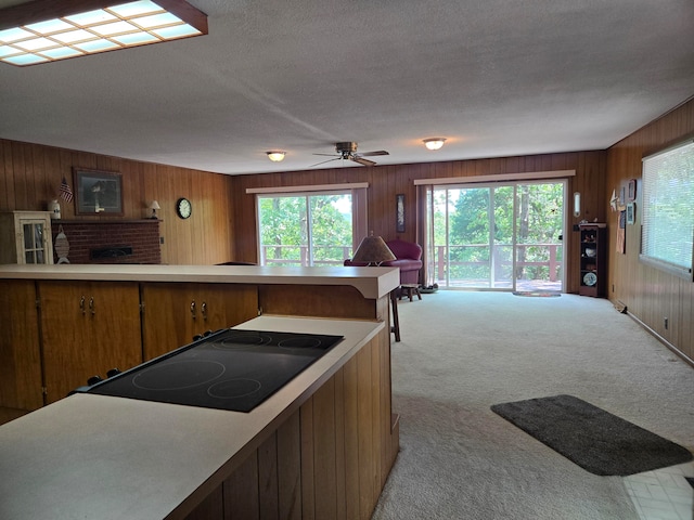 kitchen with a brick fireplace, light colored carpet, wood walls, and black electric stovetop